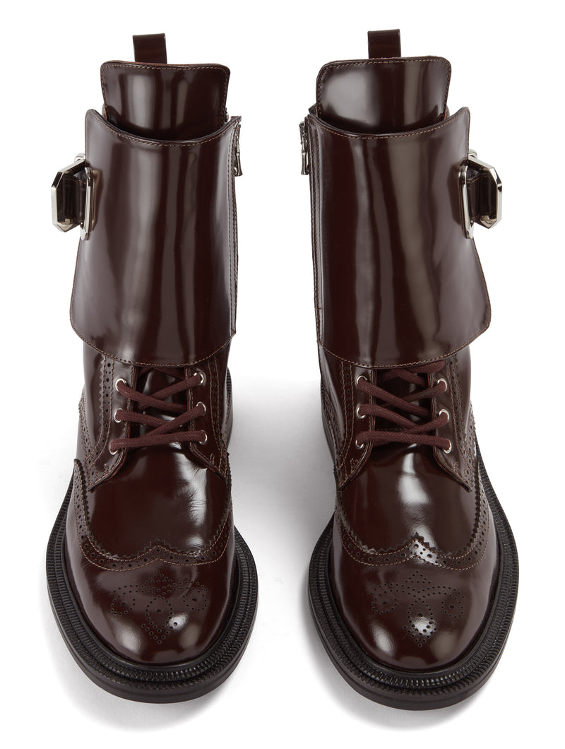 Front view of the CWEN combat boot in a brown glossed leather, brogue detail, light tan colour lining, silver buckle and a ridged rubber sole