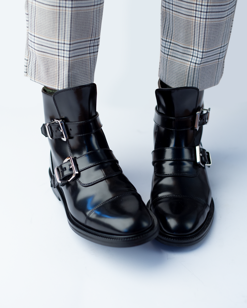 Girl feet in grey trousers and CWEN ankle glossed black boots, with two strap, light tan colour lining and a leather sole